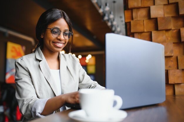 Feliz trabajadora afroamericana que usa una computadora portátil para estudiar en una computadora en una oficina de loft o una cafetería sonriente estudiante de raza mixta independiente que usa una aplicación de PC para comunicarse en línea viendo un seminario web