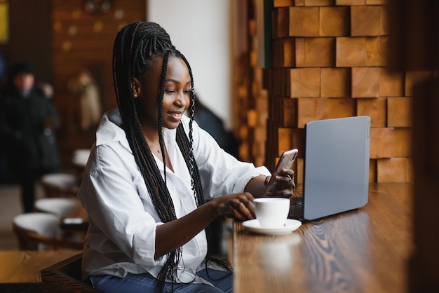 Feliz trabajadora afroamericana que usa una computadora portátil para estudiar en una computadora en una oficina o cafetería, una estudiante independiente sonriente de raza mixta que usa una aplicación de PC para comunicarse en línea viendo un seminario web