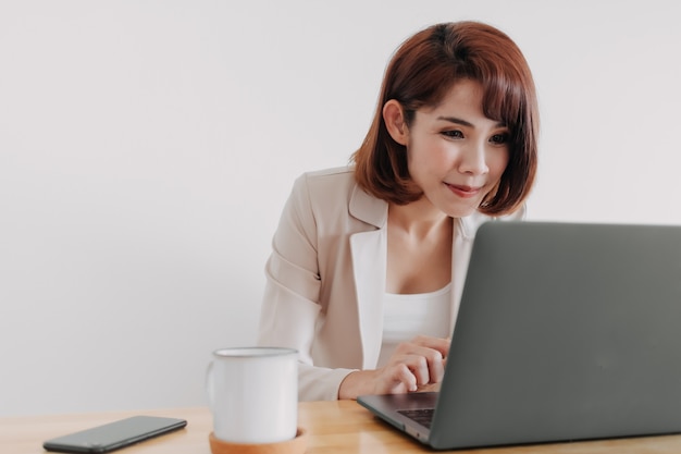 Feliz trabajadora asiática está trabajando en su computadora portátil en la oficina