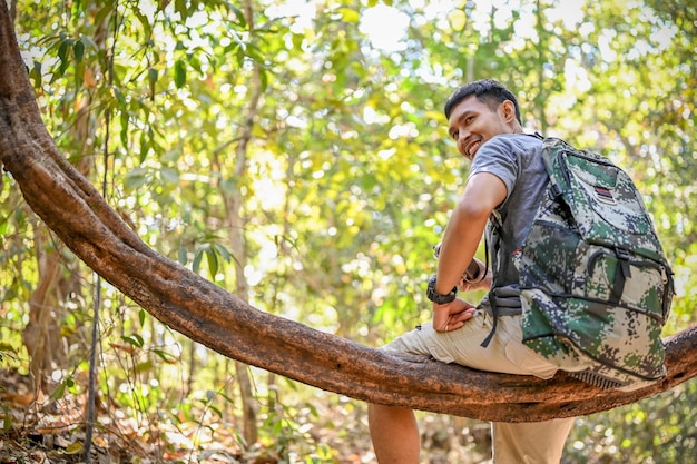Feliz trekker ou viajante asiático sentado em uma videira de madeira descansando enquanto caminhava na floresta