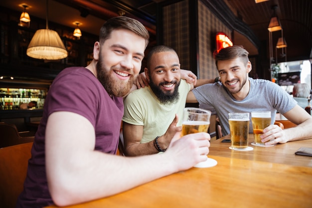 Feliz tres amigos sentados en el pub de cerveza y mirando al frente