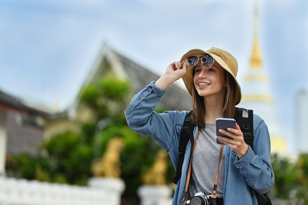 Feliz turista caucásica con mochila usando un teléfono inteligente mientras camina en la ciudad vieja de Chiang Mai en el norte de Tailandia