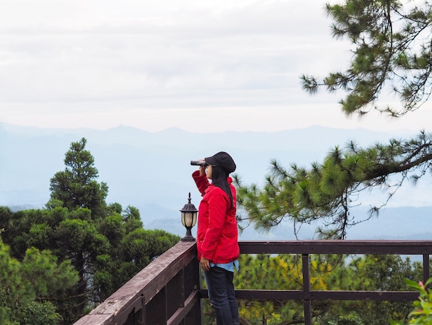 Foto feliz turista mujer asiática mirando a través de binoculares sobre mountain view con niebla en el fondo de la mañana