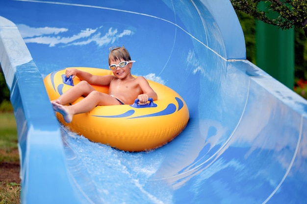 Feliz, um menino de 8 anos está andando no parque aquático em círculos infláveis em toboáguas com respingos