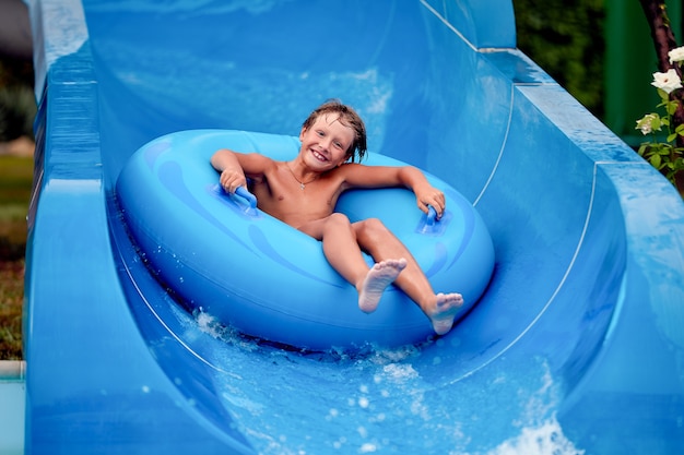 Feliz, um menino de 8 anos está andando no parque aquático em círculos infláveis em toboáguas com respingos