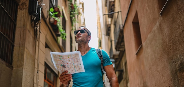 Feliz usuario de mapas turísticos masculinos caminando en el callejón del casco antiguo y usando un mapa Barcelona España