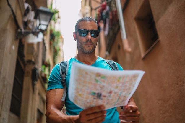 Feliz usuario de mapas turísticos masculinos caminando en el callejón del casco antiguo y usando un mapa Barcelona España