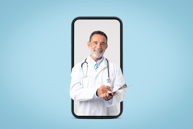 Foto feliz velho médico europeu confiante em jaleco branco com estetoscópio faz anotações na tela do telefone grande