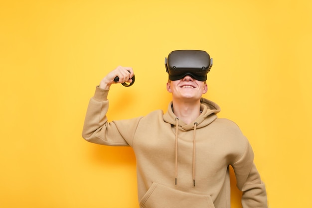 Feliz vencedor do jogador VR fica em fundo amarelo sorri e mostra bíceps Retrato de um cara em um capacete VR sorrindo isolado em amarelo Realidade Virtual Cocnept Copie o espaço