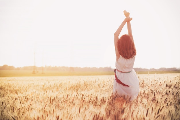 Feliz verano y libertad. Hermosa chica en el campo de trigo en un día soleado