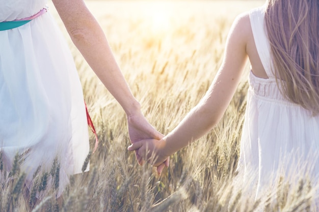 Feliz verano y vacaciones. Familia - madre con su hija cogidos de la mano en un campo de trigo