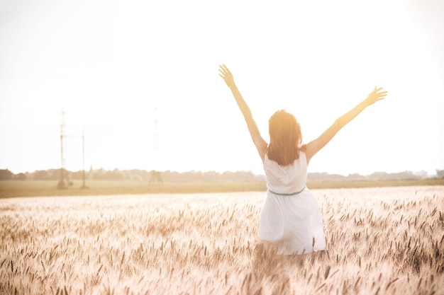 Foto feliz verão e liberdade. linda garota no campo de trigo em um dia ensolarado