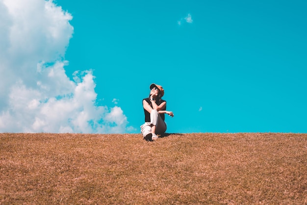 Feliz viajante asiática sentada na natureza verde com céu azul claro