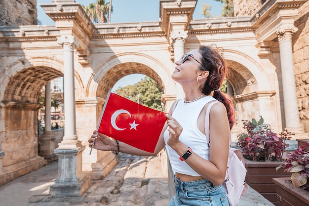Feliz viajante com bandeira turca na mão e famoso portão ou arco de Adriano no feriado nacional de Antalya e deve visitar locais turísticos e turísticos na Turquia