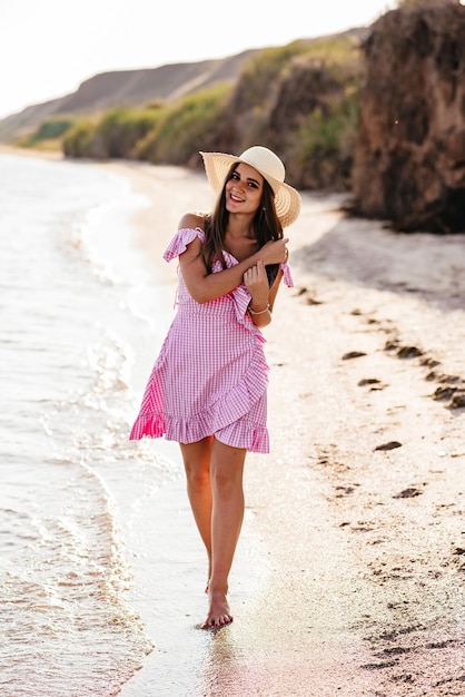 Feliz viajante de vestido branco e chapéu gosta de suas férias na praia tropical