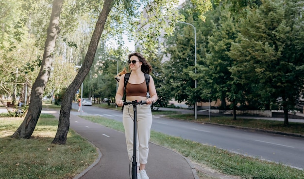 Feliz viajante sorridente está montando sua eletro scooter no parque da cidade com cachorro welsh corgi pembroke em uma mochila especial