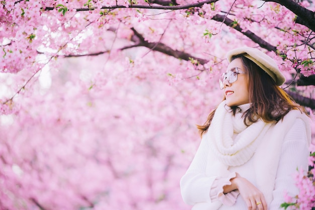 Feliz viajar mulher e sorrir com a árvore de flores de cerejeira sakura de férias durante a primavera, asiático