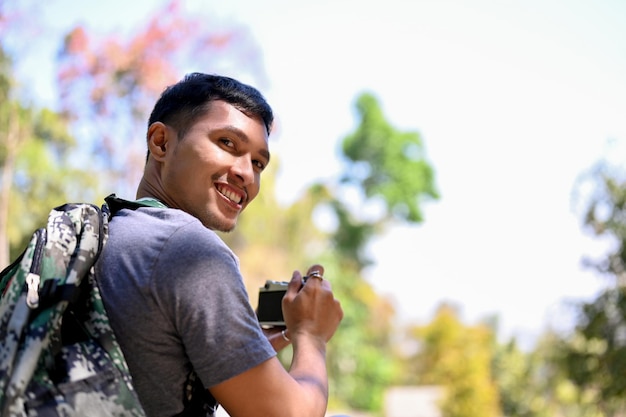 Feliz viajero asiático con mochila sosteniendo una cámara de cine sonriendo y mirando a la cámara