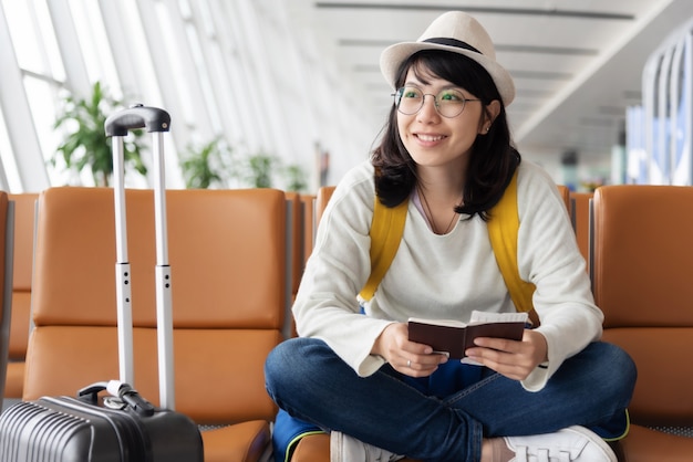 Feliz viajero de mujer asiática está esperando el vuelo en el aeropuerto.