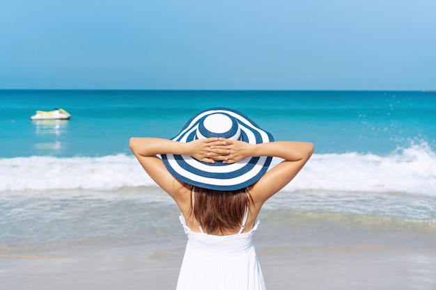 Feliz viajero mujer asiática en vestido blanco disfruta en playa tropical de vacaciones