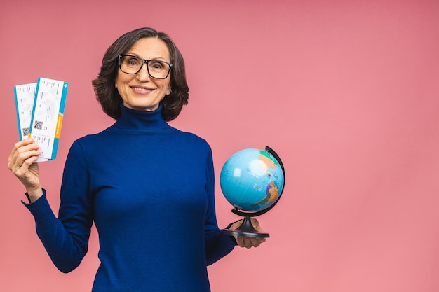 Feliz viajero turista anciana madura senior mujer sosteniendo boletos y globo aislado sobre fondo rosa studio. Los pasajeros viajan al exterior los fines de semana. Concepto de viaje de vuelo aéreo.