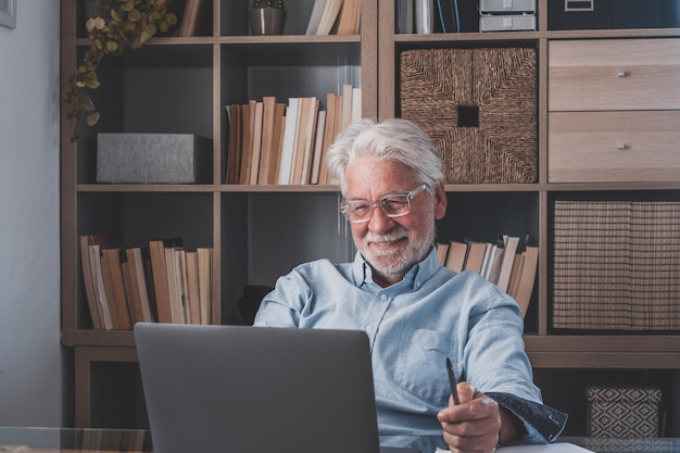 Feliz viejo hombre de negocios caucásico sonriendo trabajando en línea viendo podcast de seminarios web en una computadora portátil y aprendiendo cursos de educación llamadas en conferencia hacer notas sentarse en el escritorio elearning conceptxA