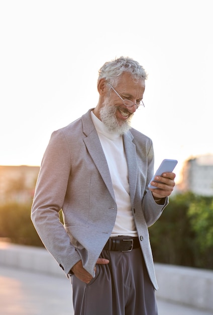 Feliz viejo hombre de negocios profesional sosteniendo usando teléfono vertical al aire libre