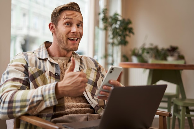 Feliz visitante de café jovem freelancer trabalhando em uma cafeteria sentado com telefone e laptop