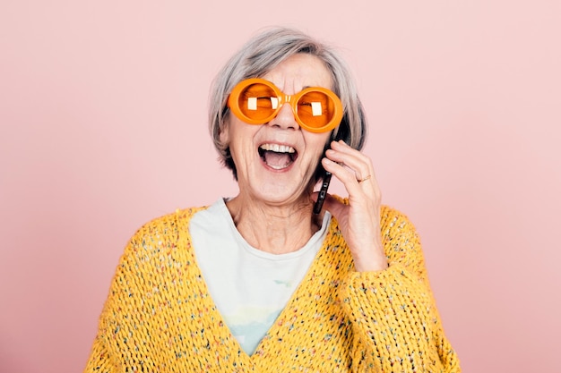 Feliz vovó idosa de estilo jovem com óculos de sol laranja e aparência moderna rindo ao telefone