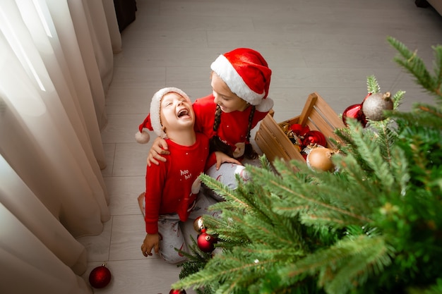 felizes abraçando irmão e irmã em pijama vermelho decoram a árvore de Natal na sala de estar