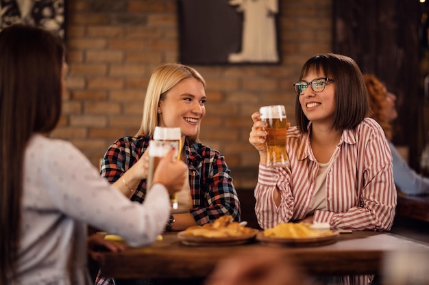 Felizes amigas brindando enquanto bebem cerveja e se reúnem em um pub