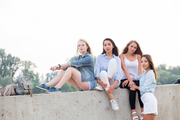 Felizes amigas fofas sentadas na borda de concreto e olhando a câmera