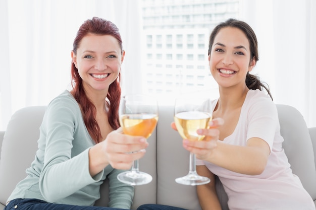 Felizes amigas segurando copos de vinho em casa