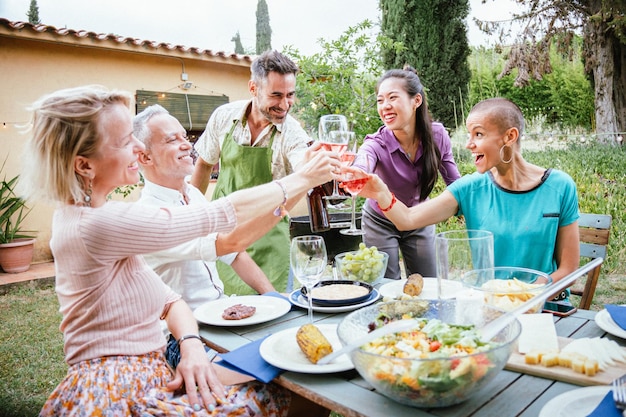 Felizes amigos adultos sorrindo e brindando com taças de vinho na celebração no quintal da casa