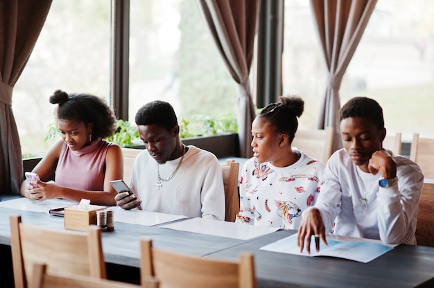 Felizes amigos africanos, sentado e conversando no café. grupo de povos negros reunidos em restaurante e olha para o seu telefone móvel.