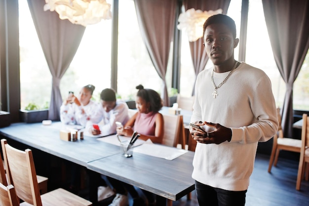 Felizes amigos africanos sentados e conversando no café Retrato de homem negro com celular nas mãos contra grupo de povos afro