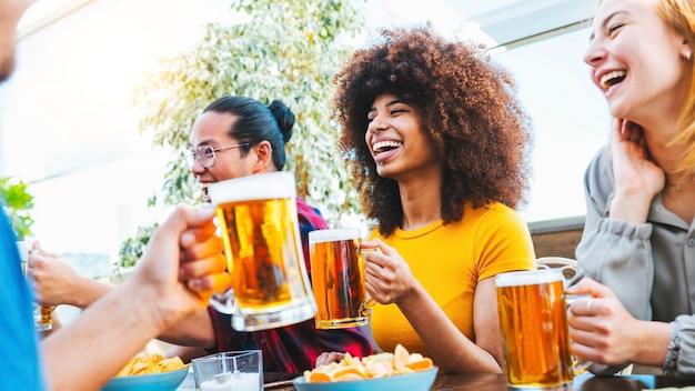 Felizes amigos multirraciais torcendo por copos de cerveja no pub da cervejaria