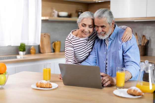 Felizes cônjuges idosos passando tempo com laptop na cozinha