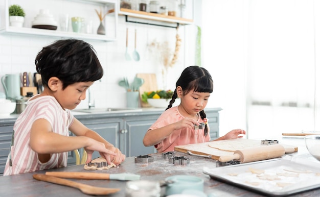 Felizes crianças engraçadas da família asiática estão preparando a massa para assar biscoitos na cozinha