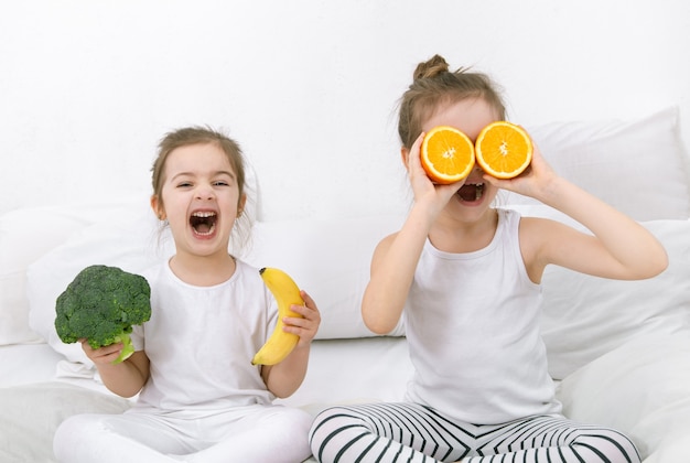 Felizes dois filhos bonitos brincam com frutas e vegetais na cama. Alimentação saudável para crianças.