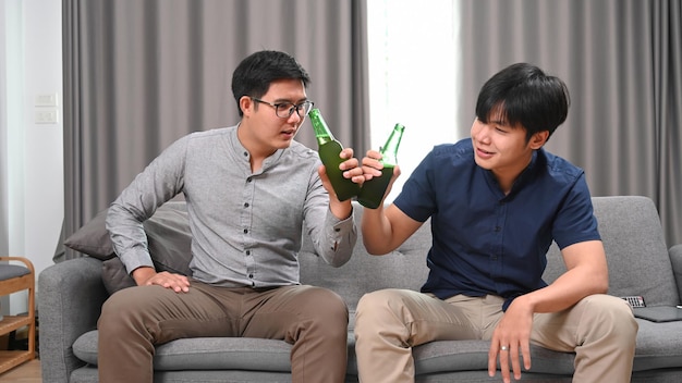 Felizes dois homens bebendo cerveja enquanto está sentado no sofá