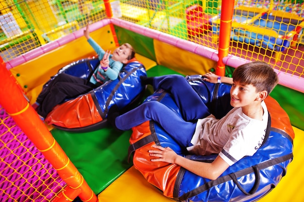 Felizes dois irmãos em rosquinhas de tubos, desfrutando de slides no centro infantil divertido.