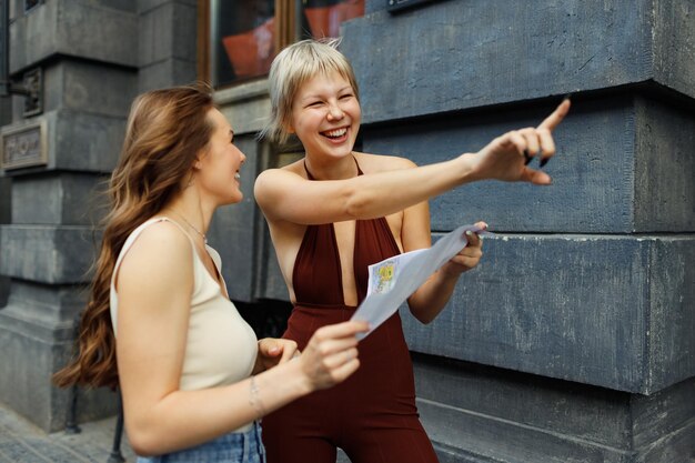 Felizes duas jovens mulheres turistas viajantes com mapa de papel está explorando nova cidade