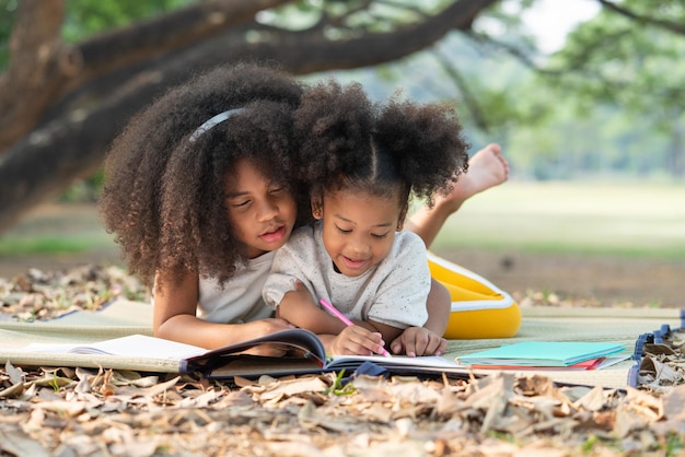 Felizes duas meninas afro-americanas deitadas desenhando no livro de colorir para crianças no parque