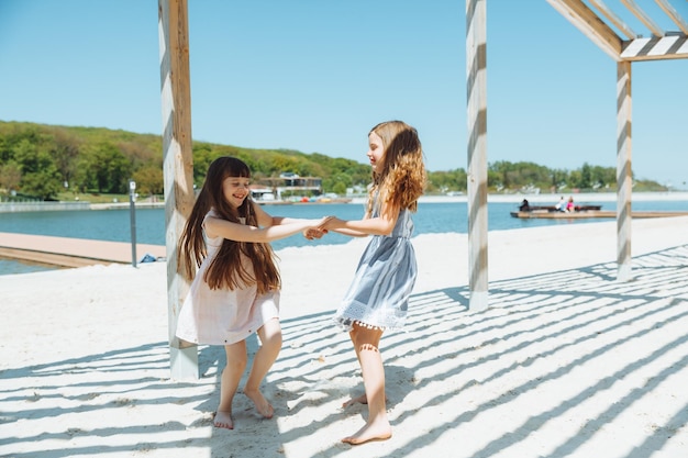 Felizes duas meninas se divertem e correm alegremente na praia pulando na areia