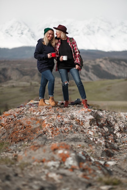 Felizes duas raparigas viajantes em pé na rocha nas montanhas