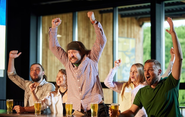Felizes e entusiasmados jovens amigos e amigas se encontrando no bar do pub assistindo a jogos esportivos online