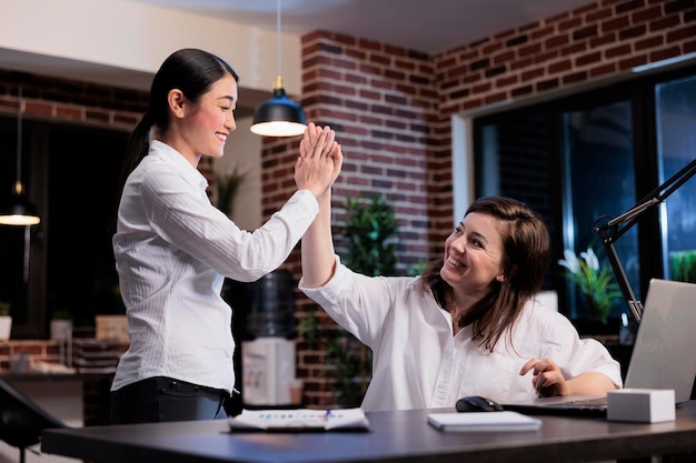 Felizes empresárias motivadas no espaço de trabalho do escritório celebrando negócios bem-sucedidos cumprimentando uns aos outros. Colegas de trabalho multiétnicos animados positivos expressando conquistas.