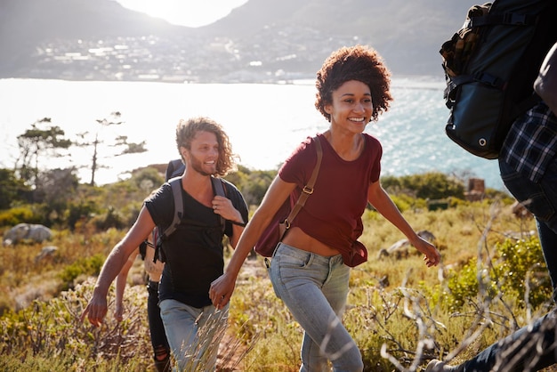 Felizes jovens amigos adultos caminhando morro acima perto da costa fecham a luz de fundo