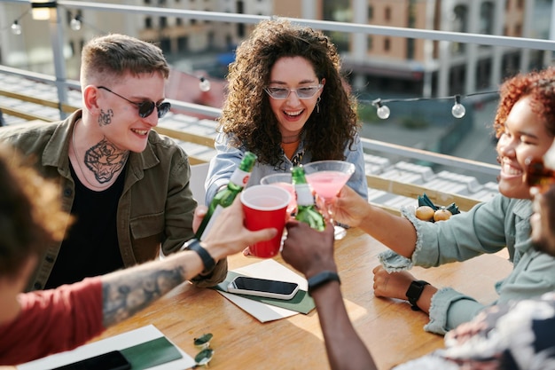 Felizes jovens amigos interraciais tinindo com suas bebidas no café ao ar livre